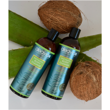 Bottle of Aleavia Enzymatic body wash laying on coconuts and aloe vera plant