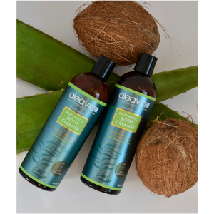 Bottle of Aleavia Enzymatic body wash laying on coconuts and aloe vera plant